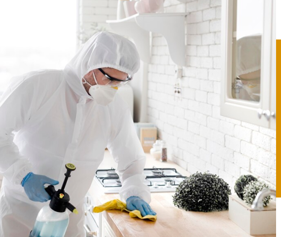 Worker in protective gear disinfecting a kitchen counter.