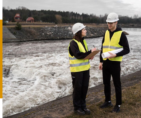 Two engineers in safety gear inspecting a riverbank.