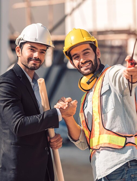 Two construction professionals shaking hands at a worksite, one in a suit and the other in safety gear.