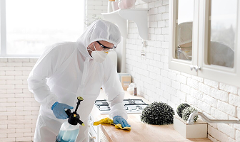 Worker in protective gear disinfecting a kitchen.