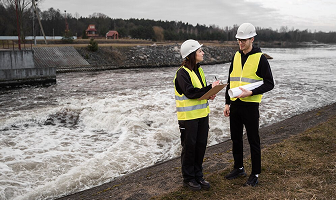Two engineers in safety gear inspecting a riverbank.